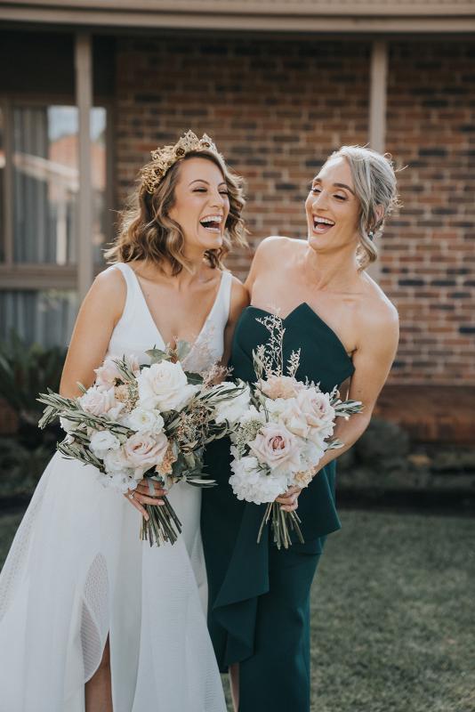 KWH real bride Talia laughing with her bridesmaid who ware a dark green dress. Talia wears the simple modern Aisha wedding dress with aline skirt.