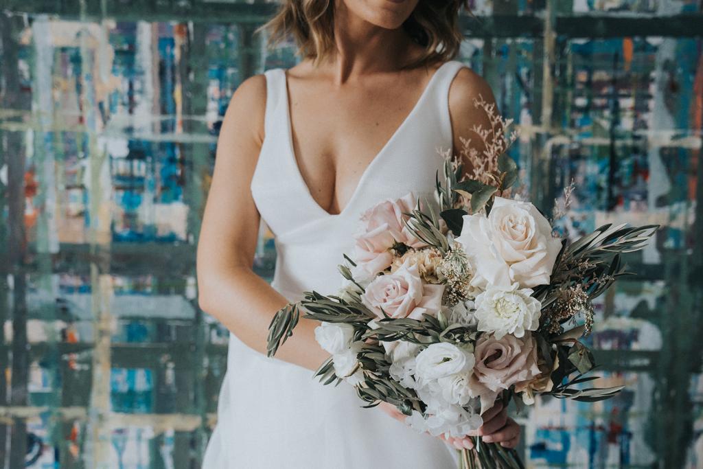 KWH real bride Talia stands with her bridal bouquet from the grounds florals by silva. She wears the modern U-shaped Aisha wedding dress.