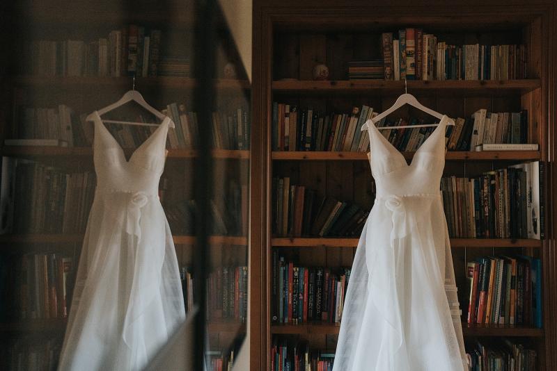 KWH real bride Talia's Aisha wedding dress hung up on a bookshelf. Aisha is a cool dress with fitted skirt and a-line overlay.