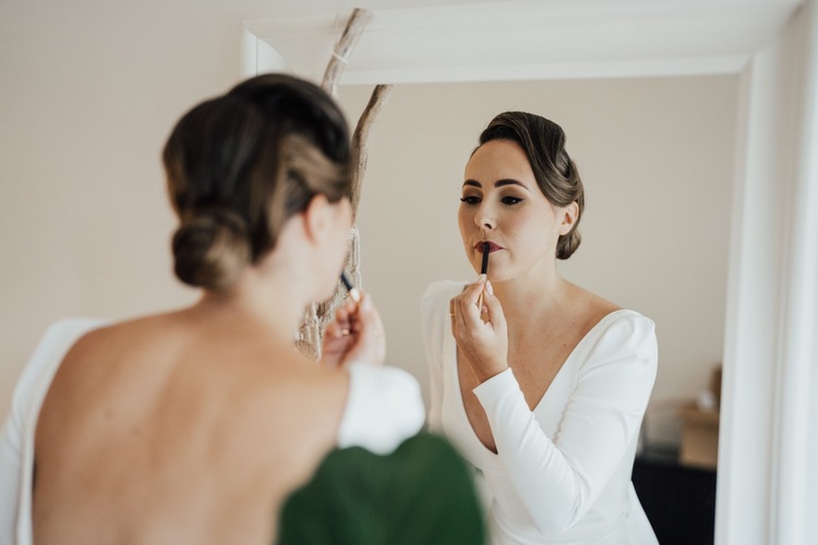 KWH real bride Jaci applying her lipstick in the mirror. She wears the classic Aubrey crepe wedding dress.