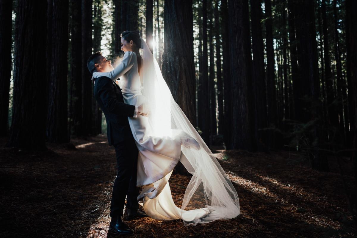 KWH real bride Jaci being pick up and spunin the woods with her new husband. She wears the comfortable Aubrey wedding dress made from crepe with a fitted silhouette.