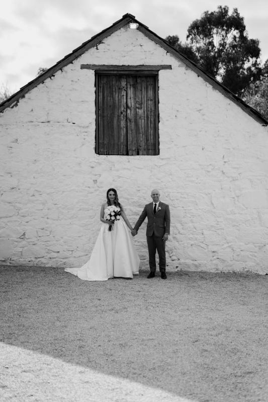 KWH real bride Elke and Kyle stand in front of a house in this B&W image. She wears the timeless Blake Camille wedding dress with bustier bodice and alien skirt.