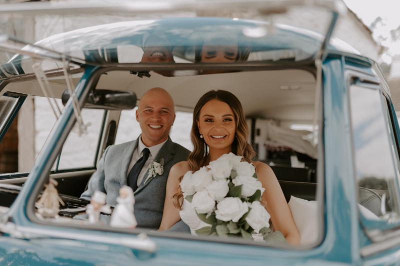 KWH real bride Elke sits in a blue volks wagen van with Kyle. She wears the modern Blake Camille wedding dress with sweetheart neckline