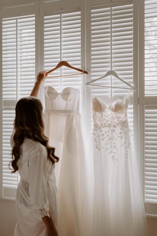 KWH real bride Elke looking at her two gowns before getting ready. Her Blake Camille custom wedding dress hangs in front of her.