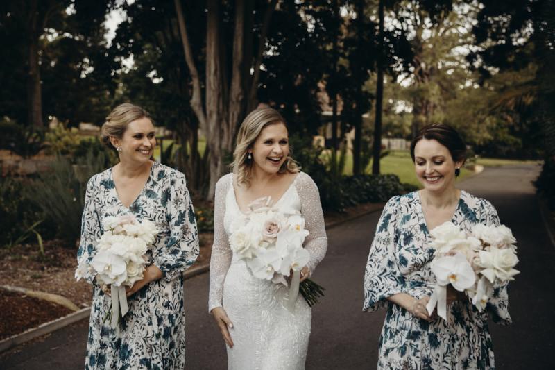 KWH real bride Emily walking with her bridesmaids who are wearing blue floral dresses. She wears the hand beaded Celine wedding dress with v-neckline