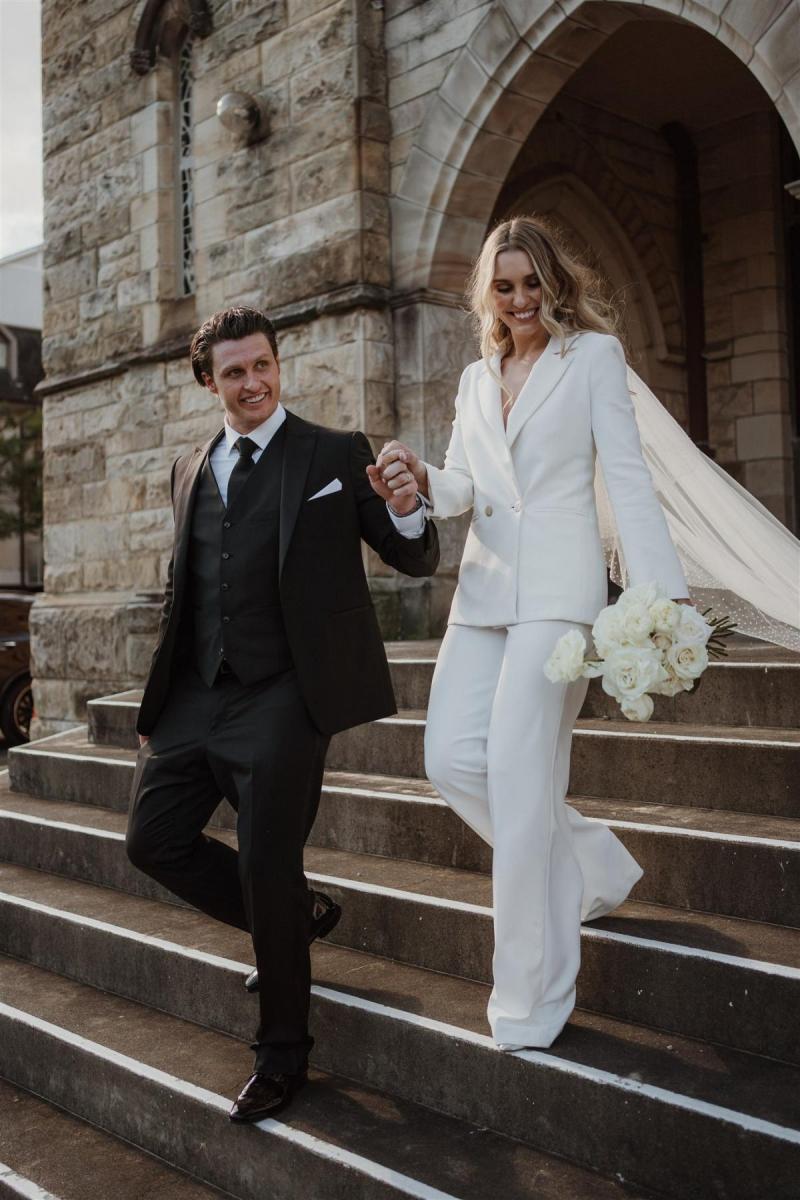 KWH real bride Demi and James walk out of the church. She wears the modern Charlie Danielle bridal suit with wide leg pant and double breasted jacket.