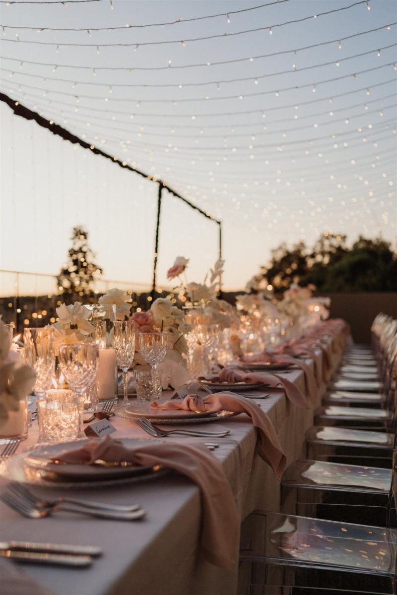 KWH real bride Demi's reception decor for their elopement with blush pinks and string lights over a long banquet table.