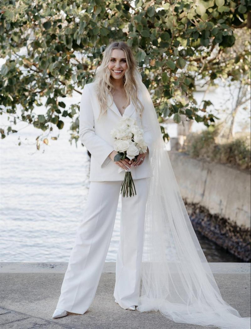 KWH real bride Demi showing off her Charlie Danielle bridal suit in front of the nearby water. She wears the classic ivory suit with straight white stem roses.