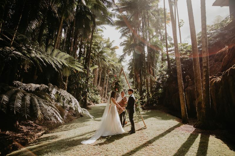 KWH real bride Jana and Garret stand at their ceremony alter in the Hawaiian rainforest. She wears the two piece Erin and Lea wedding dress with modern details.