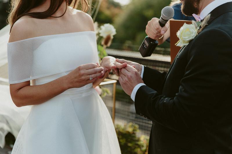 KWH real bride Libby and Luke exchanging rings. She wears the simple Esther wedding dress with mesh off the shoulder collar.