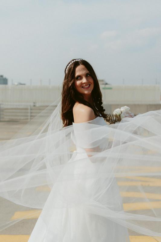 KWH real bride Libby stands in her Esther wedding dress with off the shoulder collar and aline skirt. Her veil blows in the wind
