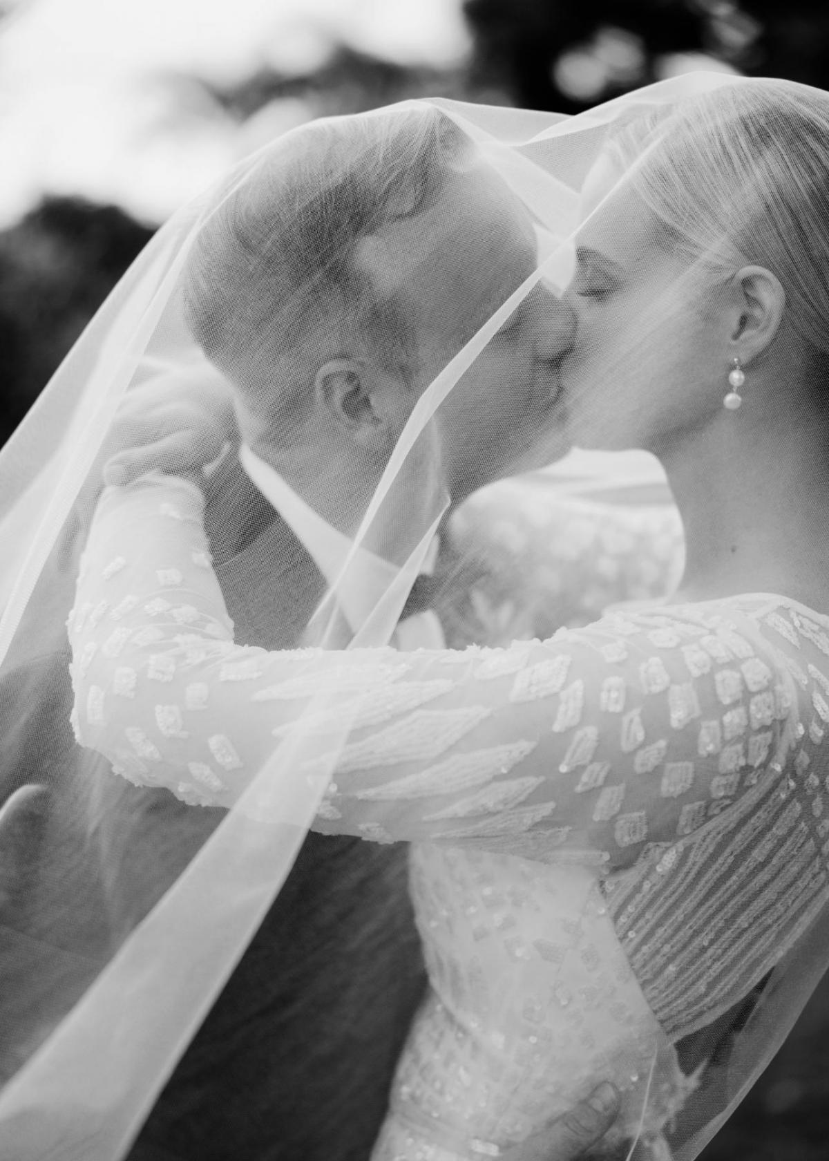 KWH real bride Taylor and Kalen kissing under her veil. She wears the long sleeved, fit and flare Lexie wedding dress.