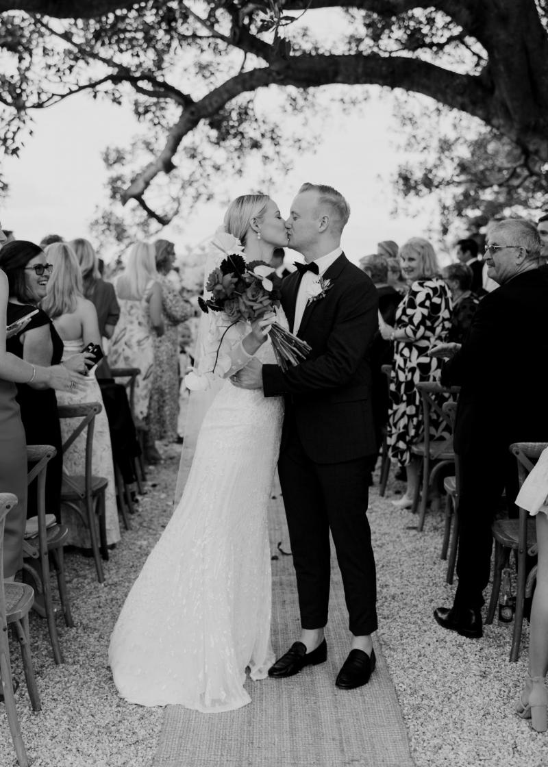 B&W image of KWH real bride Taylor and Kalen kissing in the middle of the aisle. She wears the