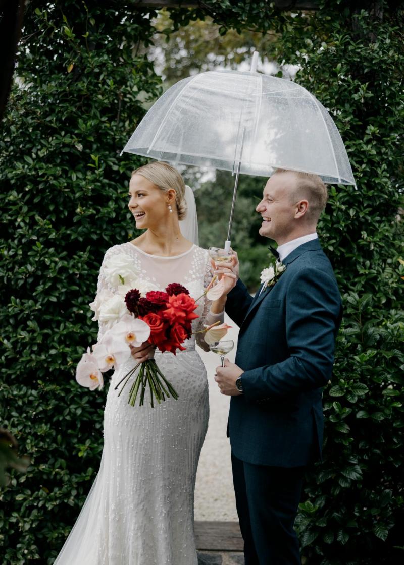 KWH real bride Taylor and Kalen under a clear umbrella. She wears the classic beaded Lexie wedding dress.