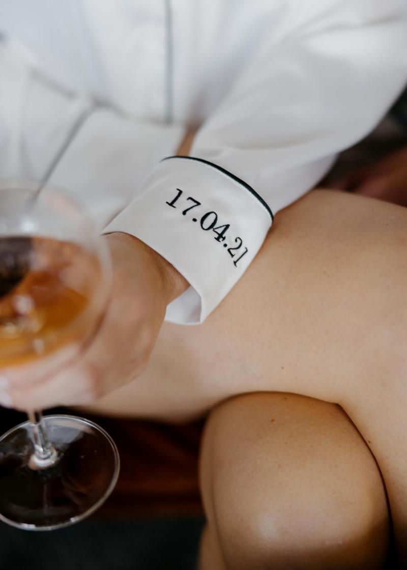 KWH real bride holding a glass in her bridal robe with wedding date embrodiered on the sleeve.