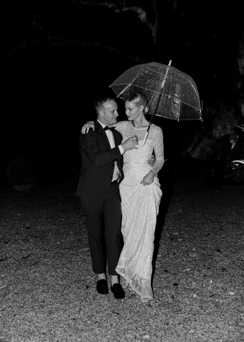 B&W image of KWH real bride Taylor and Kalen under a clear umbrella. She wears the classic Lexie gown with long sleeves.