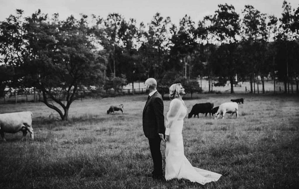 KWH real bride Caitlin and Eoin stand back to back in B&W photo. She wears the modern Penelope wedding dress with long sleeves