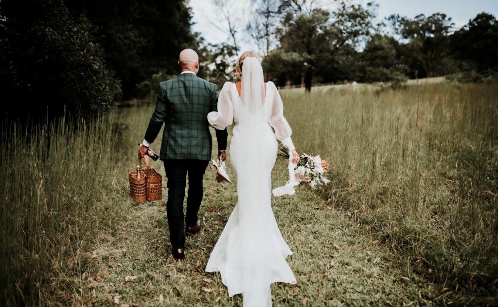 KWH real bride Caitlin and Eoin walking as he carries a case and she wears the low back Penelope wedding dress.