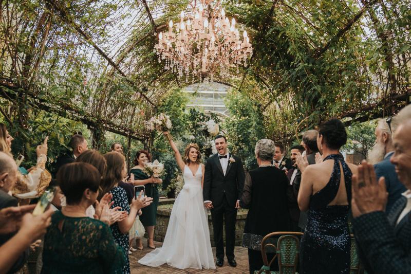 KWH real bride Talia standing under a neon sign at her reception. She wears the modern Aisha wedding dress with leg split in her aline skirt.