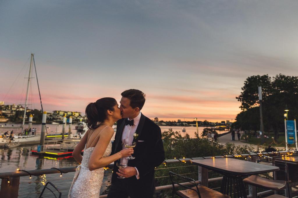KWH real bride Ash kissing Chris as the sun sets on the bay. She wears the dazzeling Anya wedding dress with all over sequins and delicate straps.