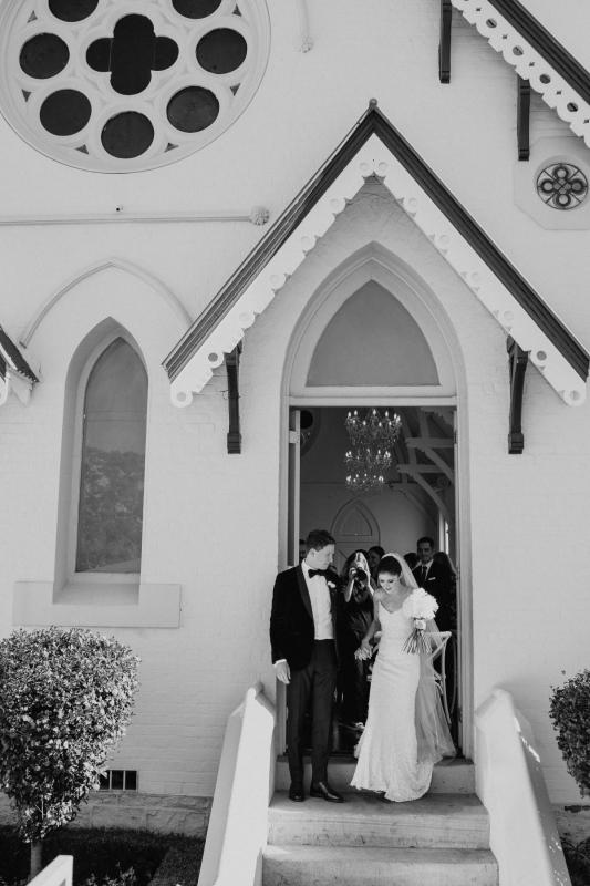 B&W image of KWH real bride Ash leaving the chapel with her new husband. She dons the minimlaist Anya sequin wedding dress.