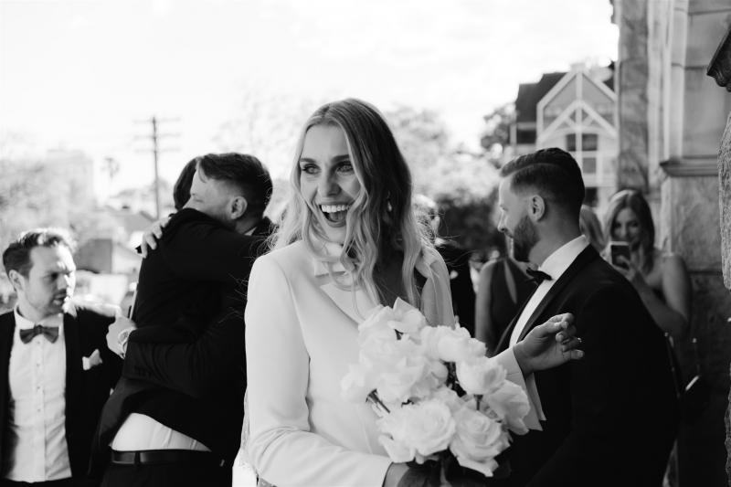 BW image of KWH real bride Demi with her white roses while wearing the classic Charlie Danielle bridal suit with flared leg.