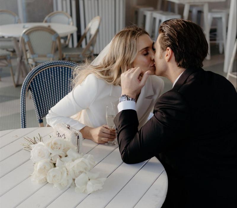 KWH real bride Demi and James have a private kiss at a cafe table. She wears the ivory Charlie Danielle bridal suit with wide leg to their city elopement