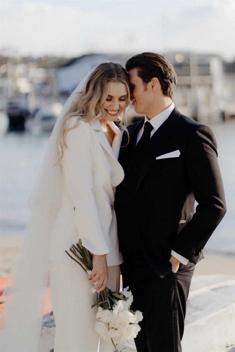 KWH real bride Demi and James hug by the Sydney harbour. She wears the minimalist Charlie Danielle bridal suit for her elopement.