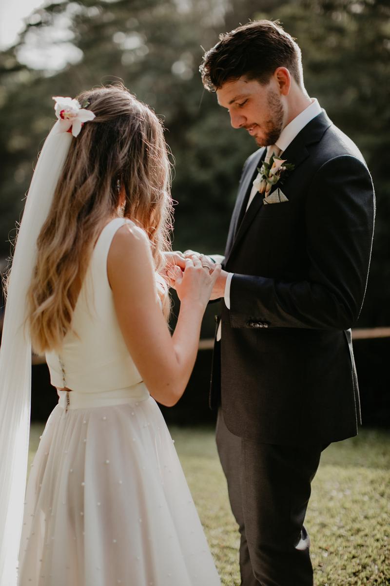KWH real bride Jana and Garret looking at their matching rings. She wears the effortless Erin and Lea two piece wedding dress with pearl details.