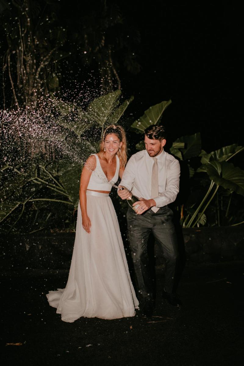 KWH real bride Jana and Garret popping a bottle of champagne. She wears the two piece Erin and Lea bridal combo featuring an aline skirt and fitted vneck bodice.