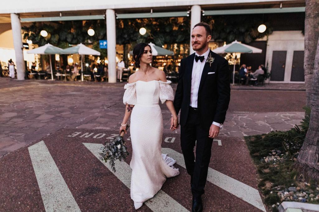 KWH real bride Tess walking across a Brisbane steet with Liam in her fitted Vivienne wedding dress for her small wedding.