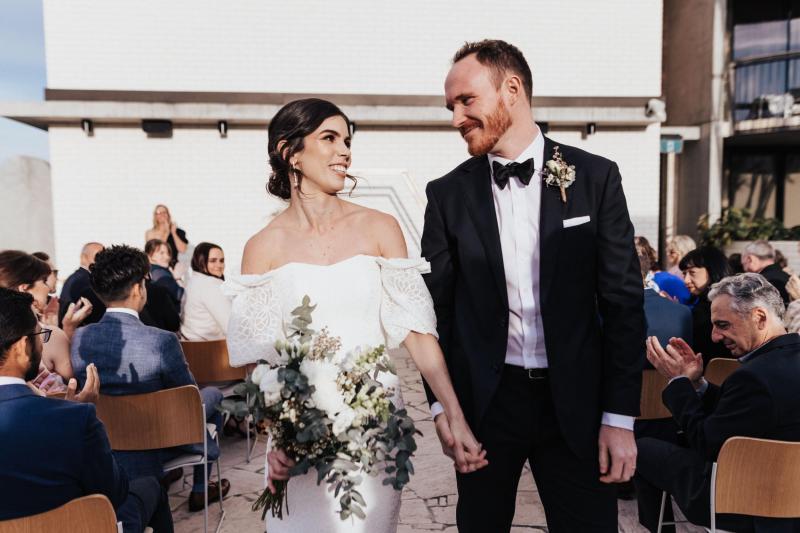 KWH real bride Tess walking down the aisle with Liam. She dons the simple lace Vivienne wedding dress with short sleeves.