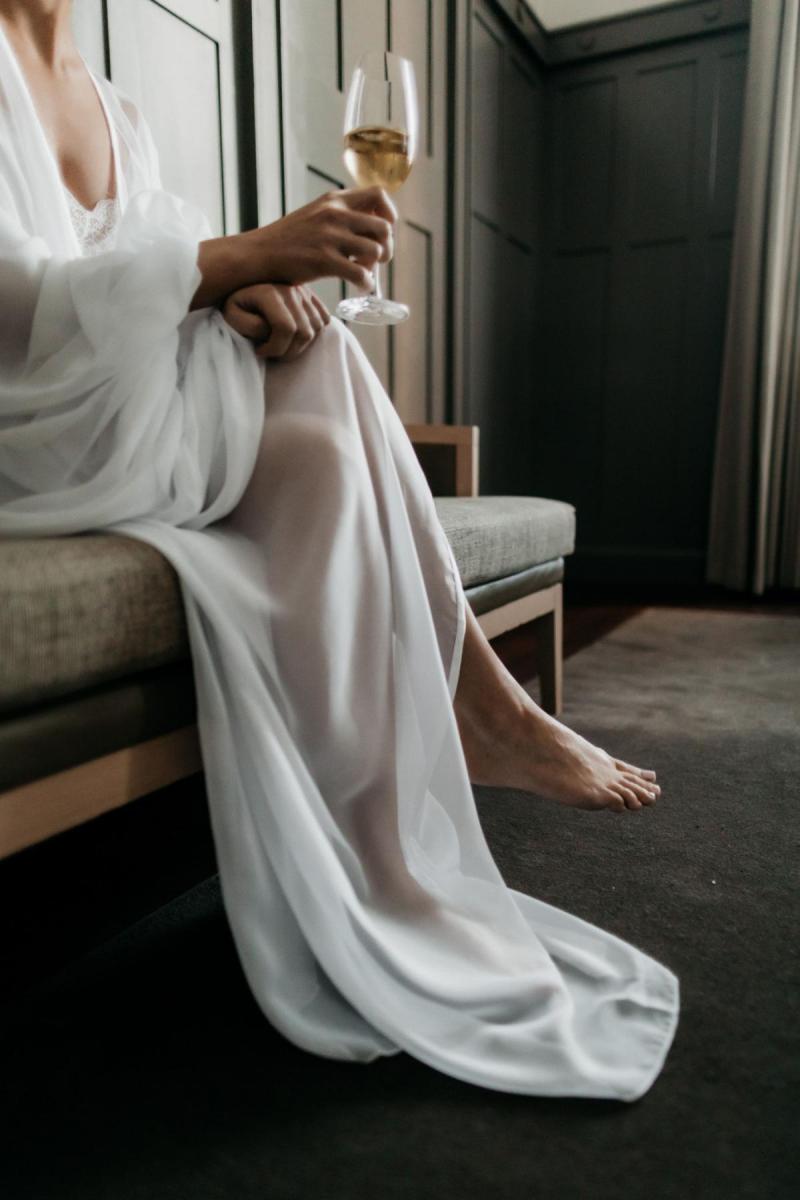 KWH real bride Genevieve sits in her bridal robe with champagne in hand as she gets ready for her outdoor wedding.