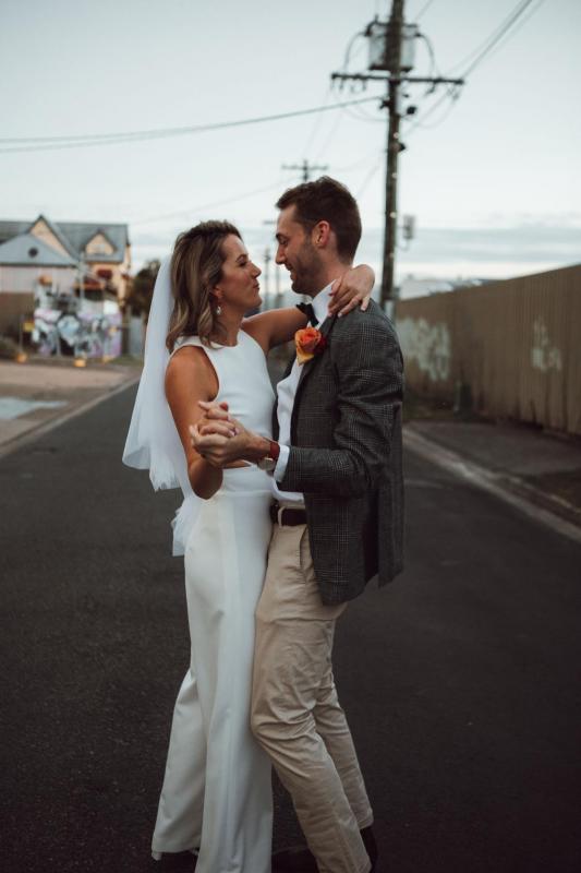 KWH real bride Casey dances in the street with her new hubby as she wears the modern Bardot bridal jumpsuit with a short veil.