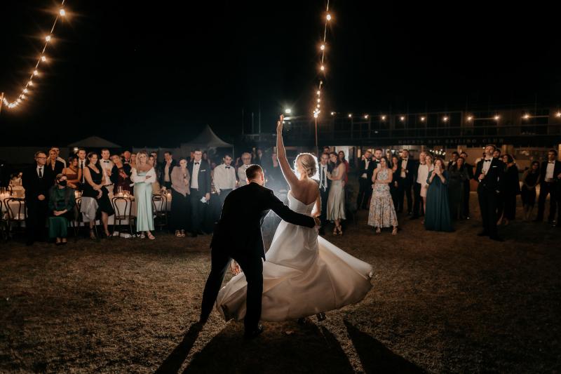 KWH real bride Genevieve and Kyle dance under the lights at their outdoor wedding. She wears the classic a-line Blake Camille wedding dress