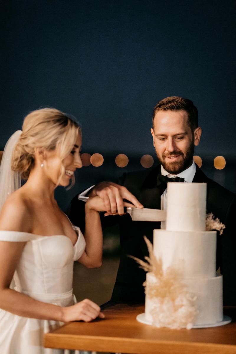 KWH real bride Genevieve cuts the cake with Kyle. She wears the bustier Blake Camille wedding dress.