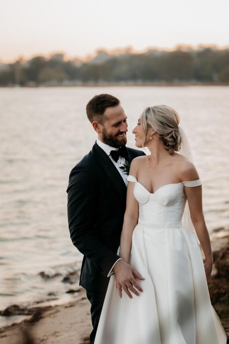 KWH real bride Genevieve and Kyle stand on the shorline of the Perth river. She wears the timeless Blake Camille wedding dress with bustier bodice and aline skirt.