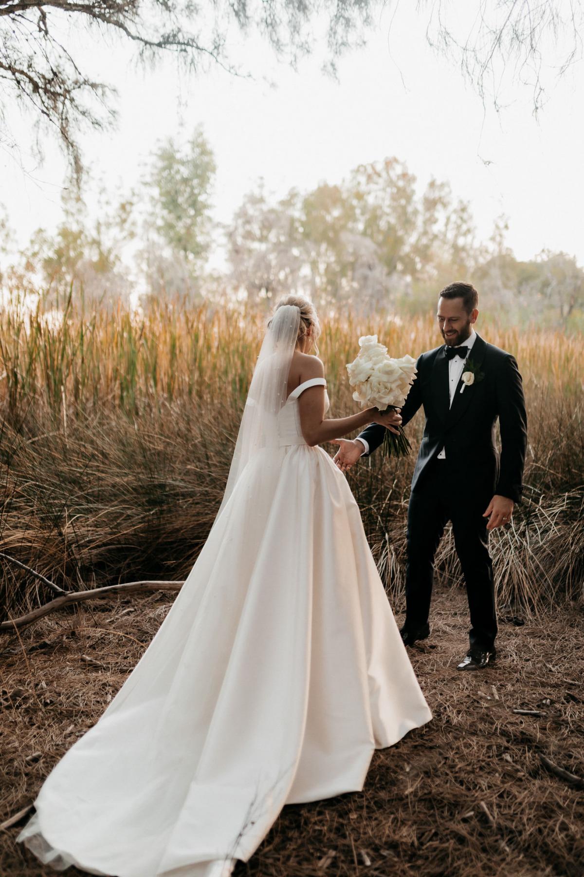 KWH real bride Genevieve and Kyle have their first look in a field. She wears the gorgeous Blake Camille wedding dress with long train and pearl veil.