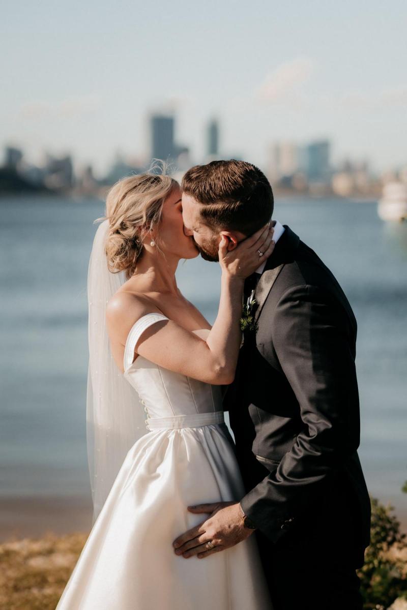 KWH real bride Genevieve kisses her new husband at their outdoor ceremony. She wears the classic Blake Camille wedding dress with off the shoulder straps.