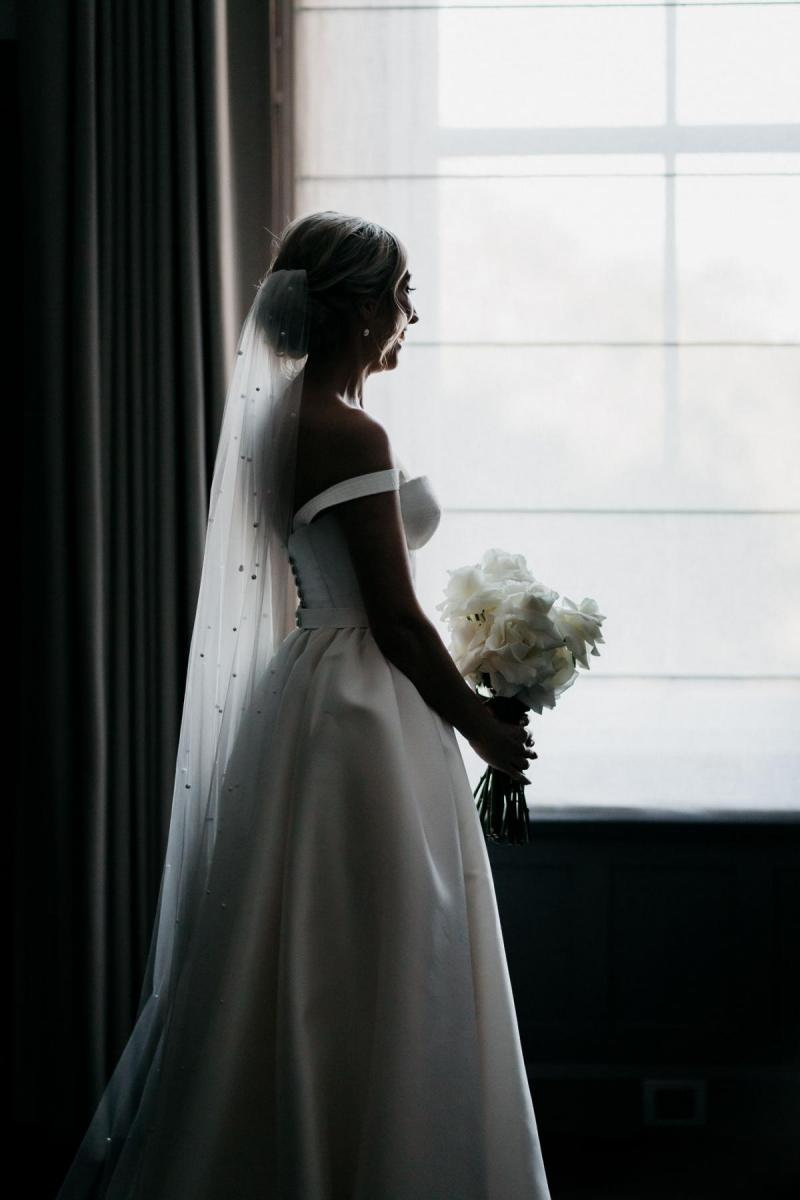 KWH real bride Genevieve by the window wearing her A-line wedding dress, Blake Camille, with bustier bodice and pearl veil'.