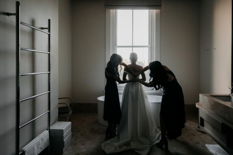 KWH real bride Genevieve has her bridesmaids help her do up her satin buttons on her Blake Camille wedding dress; a classic aline gown with bustier bodice.