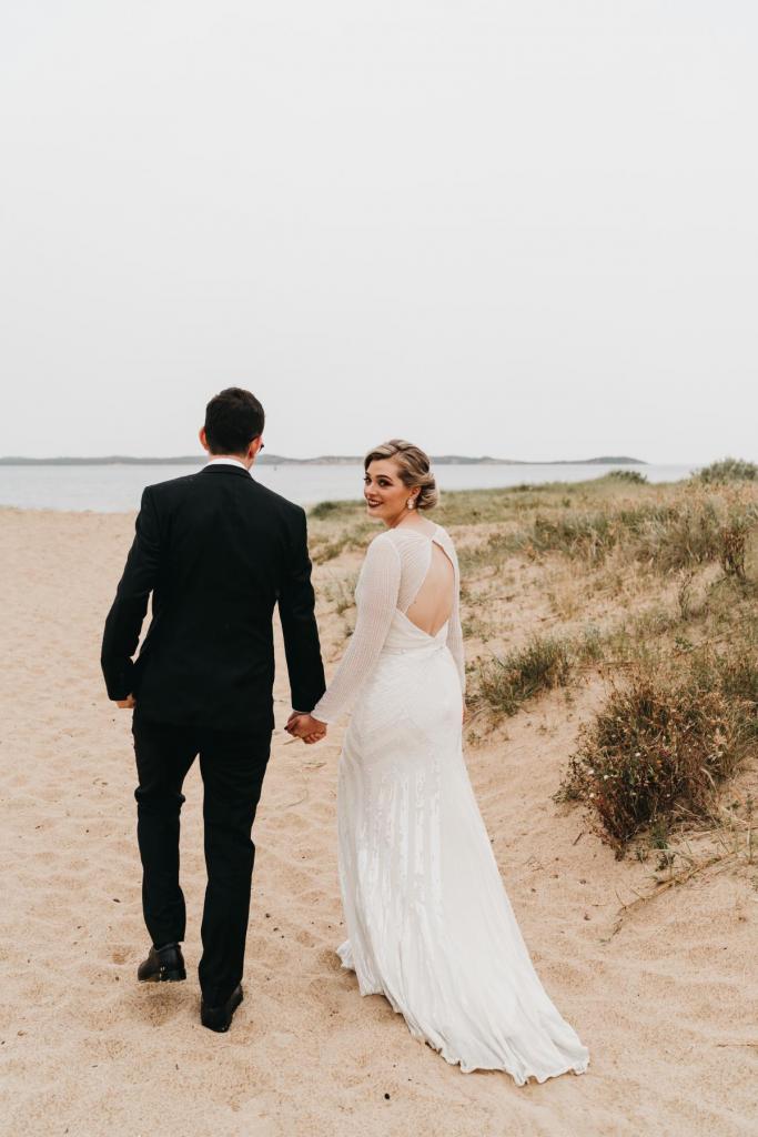 KWH real bride Nicola and Chris walk onto the nearby Melbourne beach. She wears the stunning Cassie gown; a beaded, long sleeve wedding dress with keyhole back.