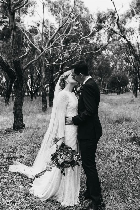 KWH real bride Nicola kisses Chris in the woods in her fitted Cassie wedding dress; a long sleeve, beaded, wedding dress.