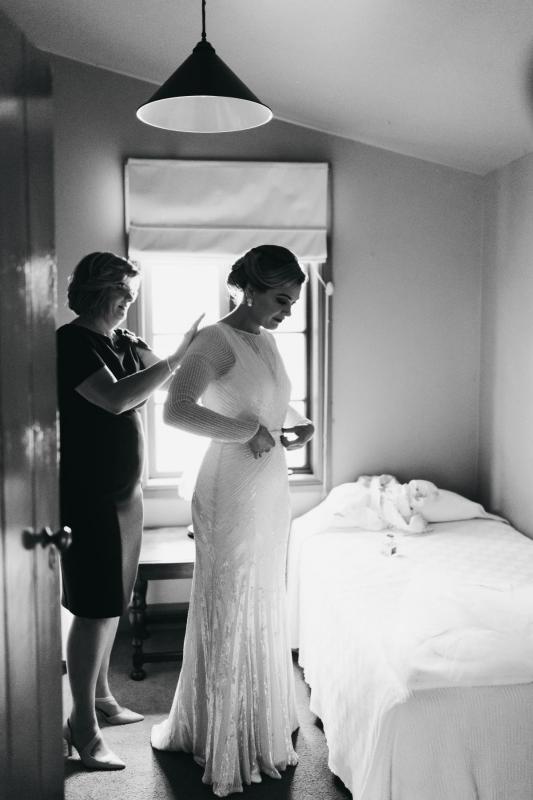 B&W image of KWH real bride Nicola's mom helping her put on her Cassie wedding dress; a high neck, hand beaded, wedding dress.