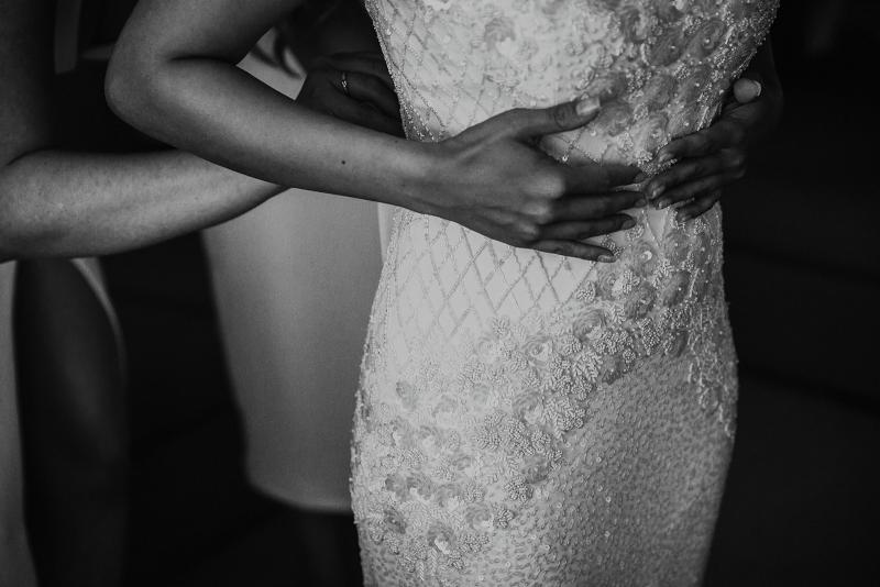 B&W image of KWH real bride Jaz putting on her Darcy gown, a hand-beaded spaghetti strap wedding dress