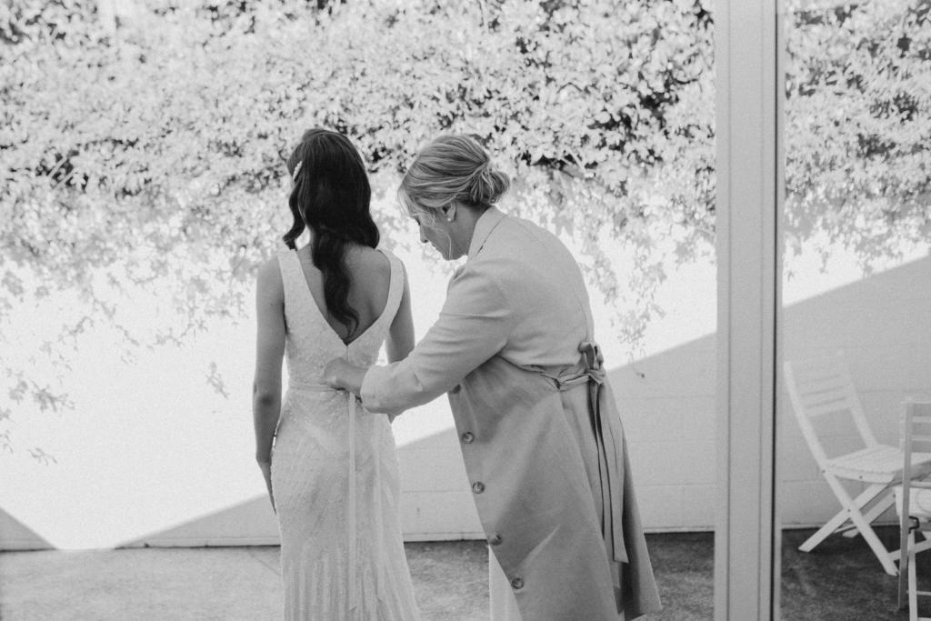 KWH real bride Georgie has her mom fasten her beaded belt to her Fontanne wedding dress; a LUXE hand-beaded wedding dress with V-neckline