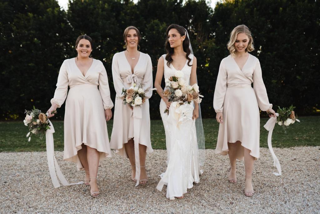 KWH real bride Georgie walking with her bridesmaids who are wearing light pink silk dresses. She wears the LUXE Fontanne wedding dress, a sequin gown.