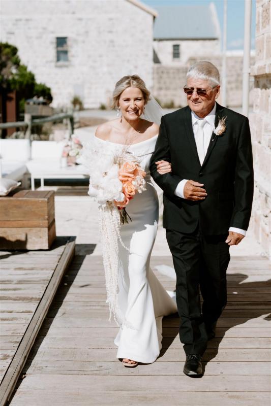KWH real bride Shelley walks down the aisle with her dad. She wears the elegant Lauren wedding dress with fold over neckline made of crepe.