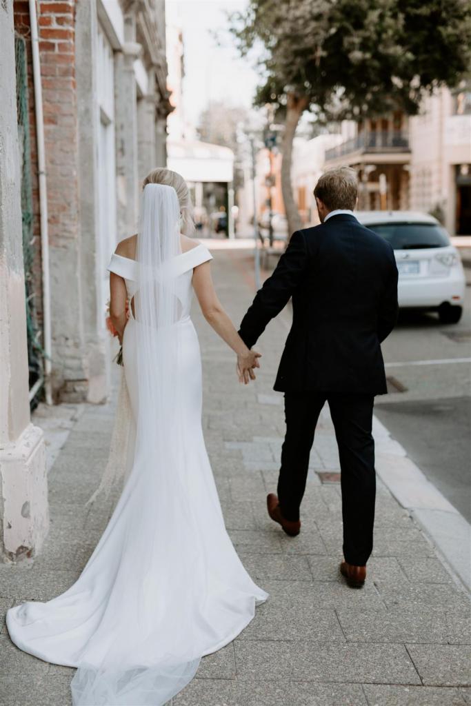 KWH real bride Shelley walks down the street with Jack. She wears the classic Lauren wedding dress with the long simple Claude veil.