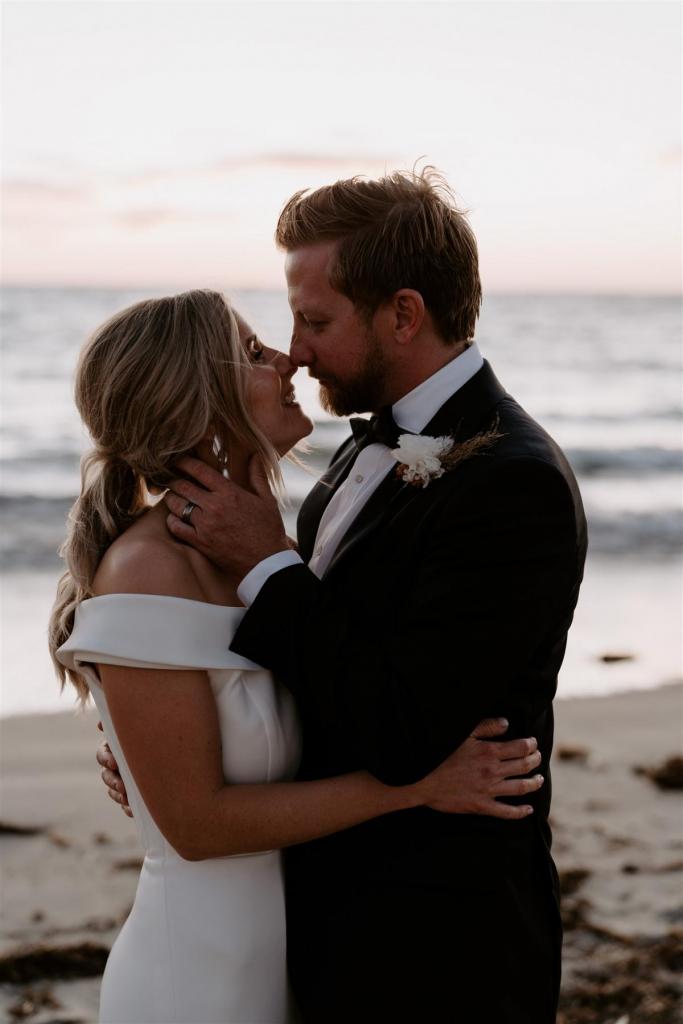 KWH real bride Shelley getts kissed by her new husband Jack on the beach. She wears the off the shoulder Lauren wedding dress.
